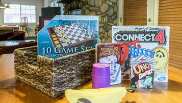 A variety of board games including chess, Connect 4, and UNO, arranged on a wooden table in a room with a stone wall and a window with blinds.