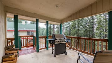 A covered outdoor area with a grill, seating, and a view of a forest.