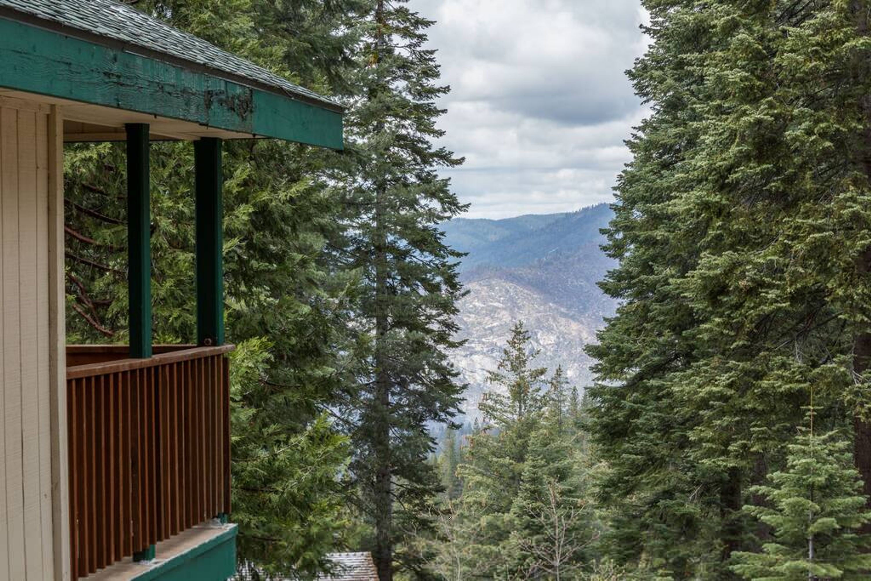 A wooden deck with a view of dense forest and distant mountains.