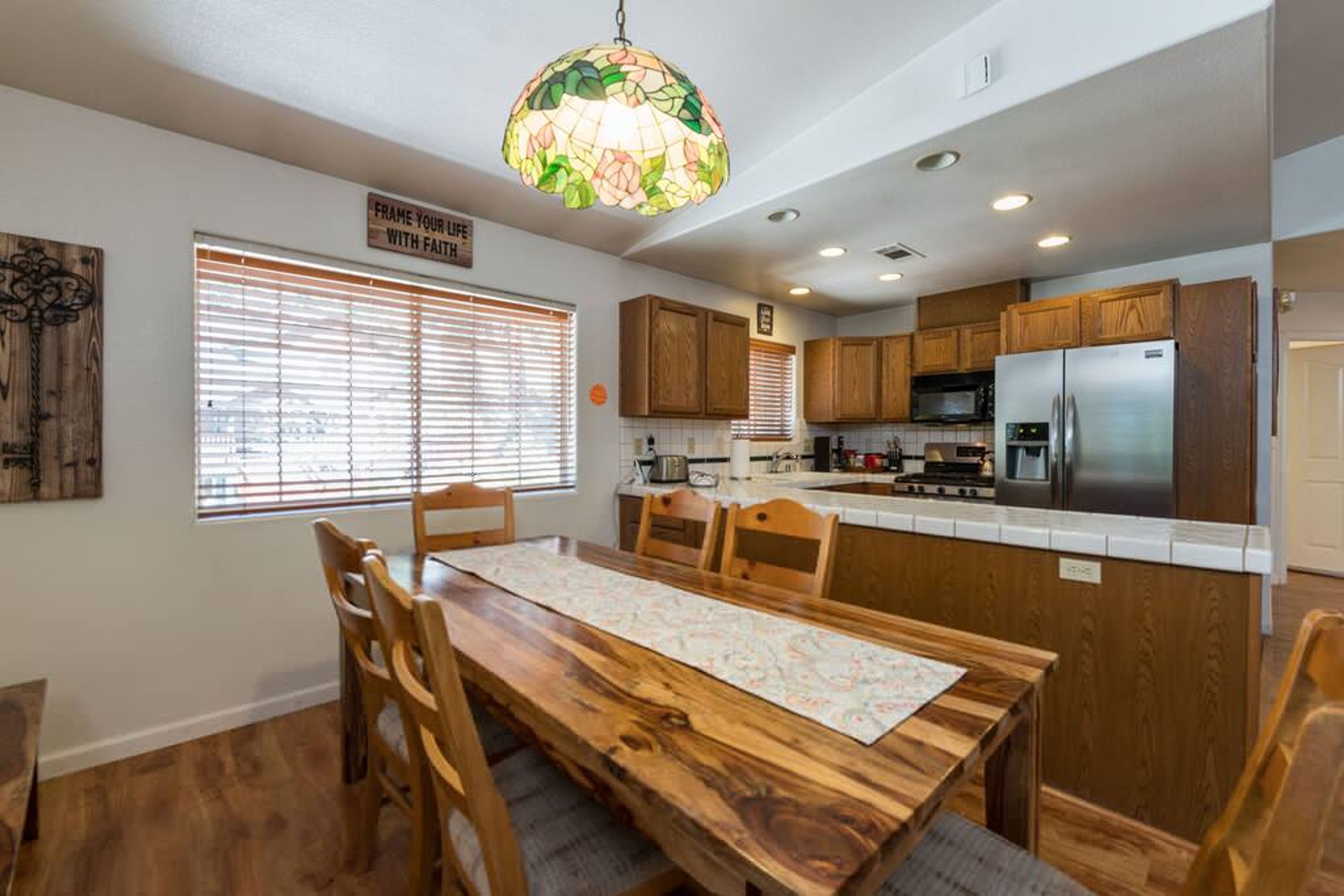 A kitchen with wooden cabinets, a stainless steel refrigerator, and a dining area with a wooden table and chairs.