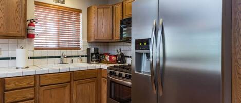 A kitchen with wooden cabinets, a stainless steel refrigerator, a stove, and a window with blinds.