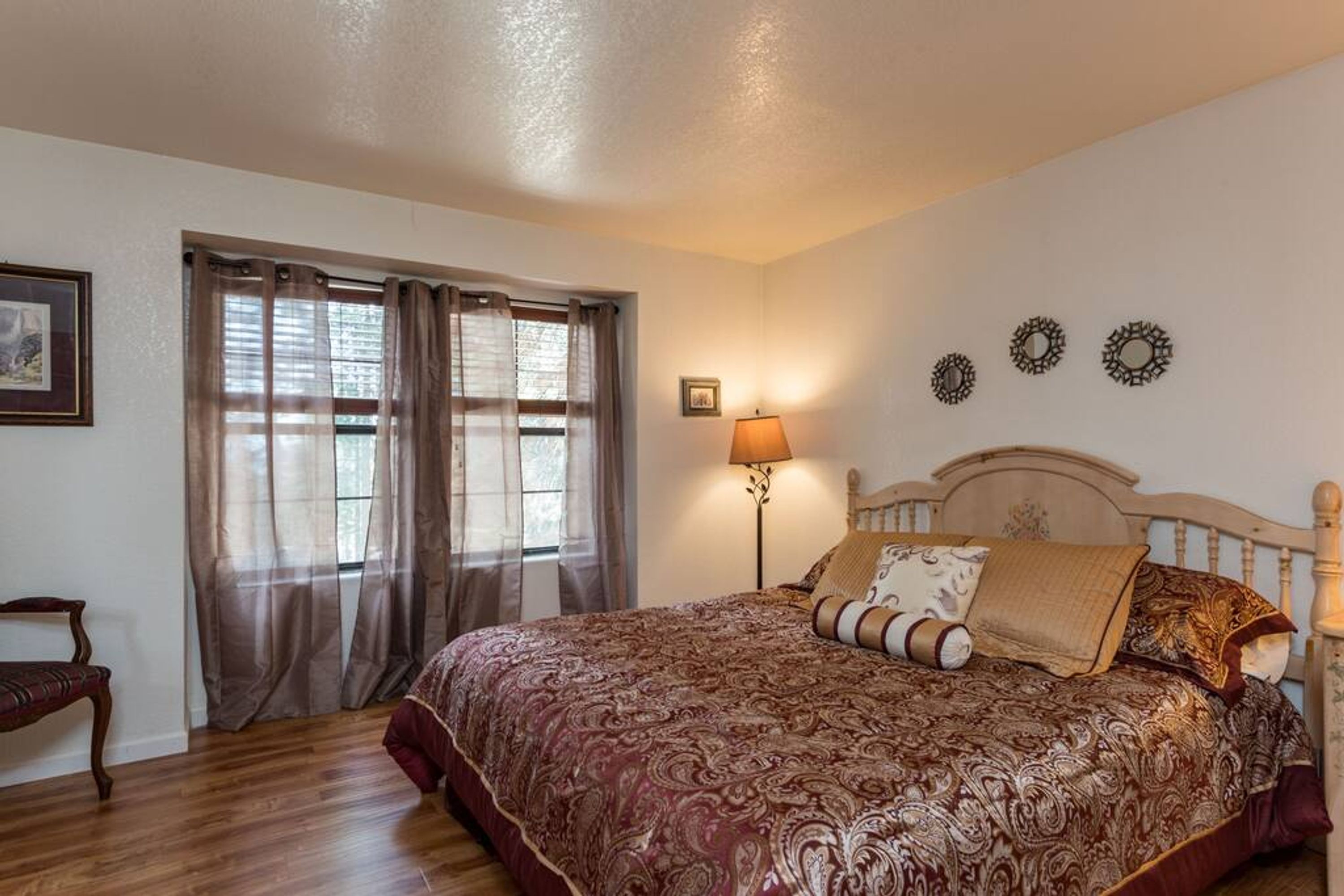 Quarto com cama grande, mesa de cabeceira, luminária e janela com cortinas.