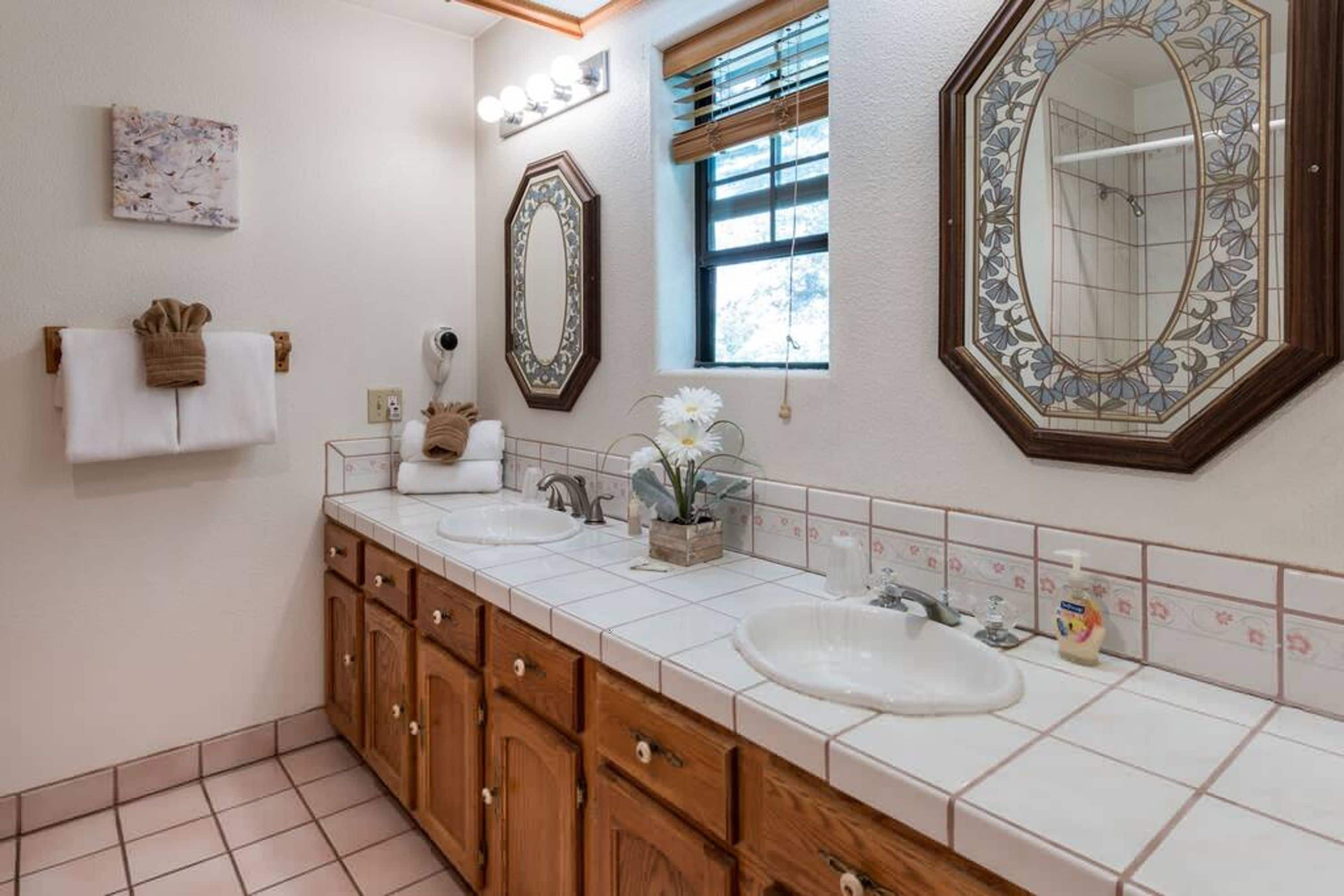 Un baño con lavamanos doble, armarios de madera, un espejo grande y una ventana con persianas.