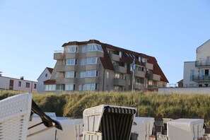 A multi-story building with balconies, a clear sky, and beach chairs in the foreground. - Beach Villa Marina 18 (Wangerooge)