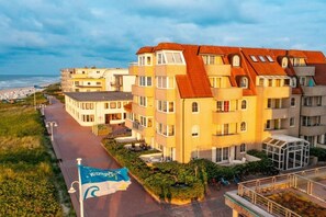 A coastal hotel with multiple balconies, a flag, and a view of the beach. - Beach Villa Marina 18 (Wangerooge)
