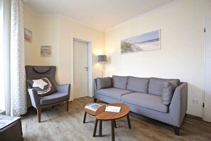 A living room with a grey sofa, a dark armchair, and a small wooden coffee table. - Beach Villa Marina 18 (Wangerooge)