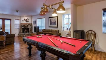 A pool table in a room with a stone fireplace, wooden flooring, and a chandelier.