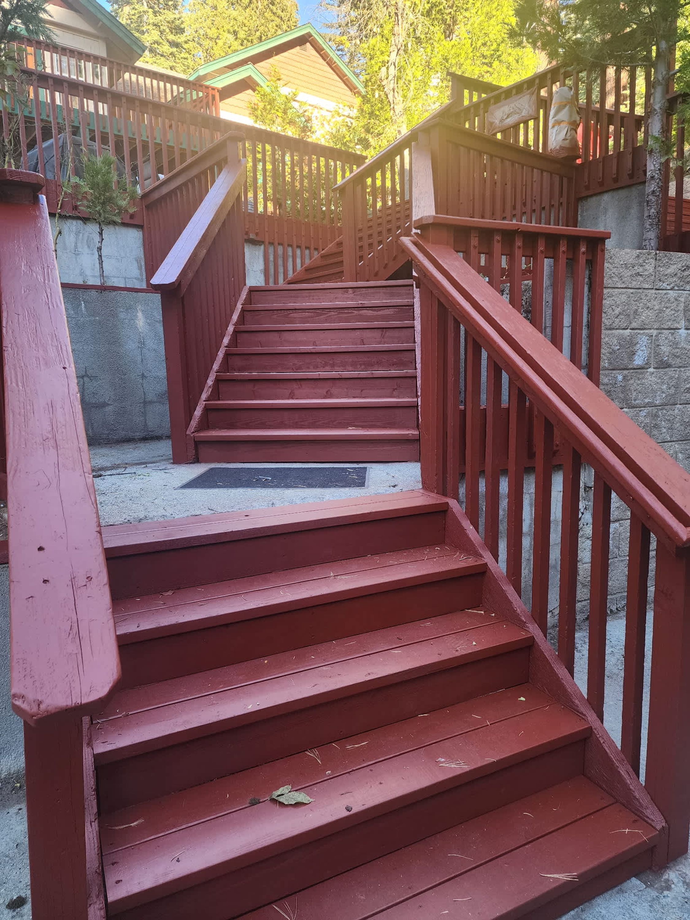 Unos escalones de madera roja con barandilla de metal, que conducen a un área cubierta con techo verde.