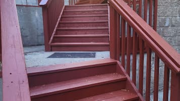 A set of red wooden stairs with a metal railing, leading to a covered area with a green roof.