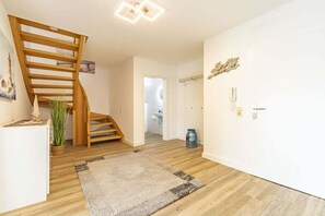 A modern interior with a wooden staircase, a white wall with a decorative piece, and a door with a light switch. - View of the dike to the right (Norddeich)