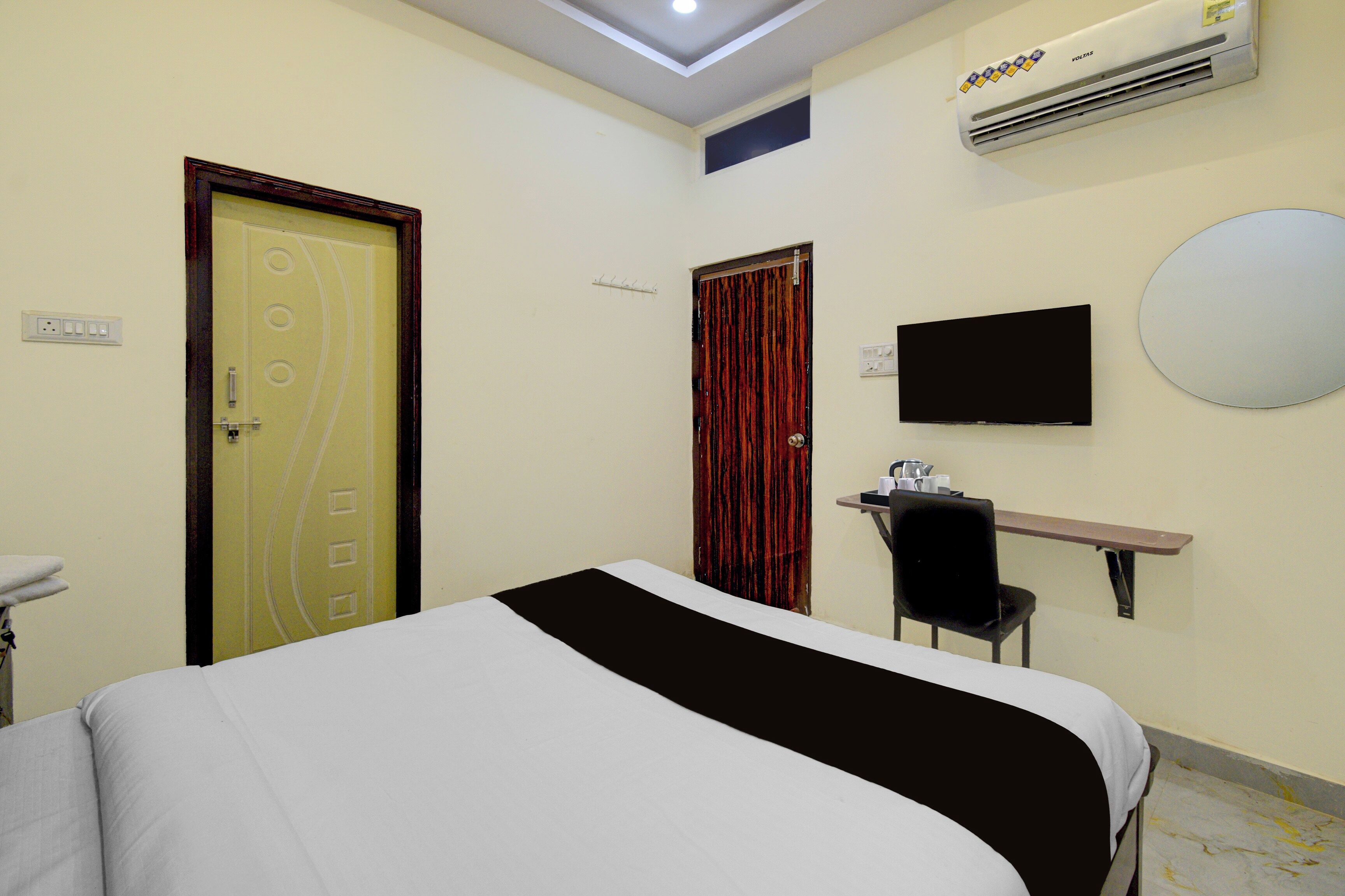 A hotel room with a bed, a desk with a chair, a television, and an air conditioning unit.