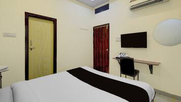 A hotel room with a bed, a desk with a chair, a television, and an air conditioning unit.