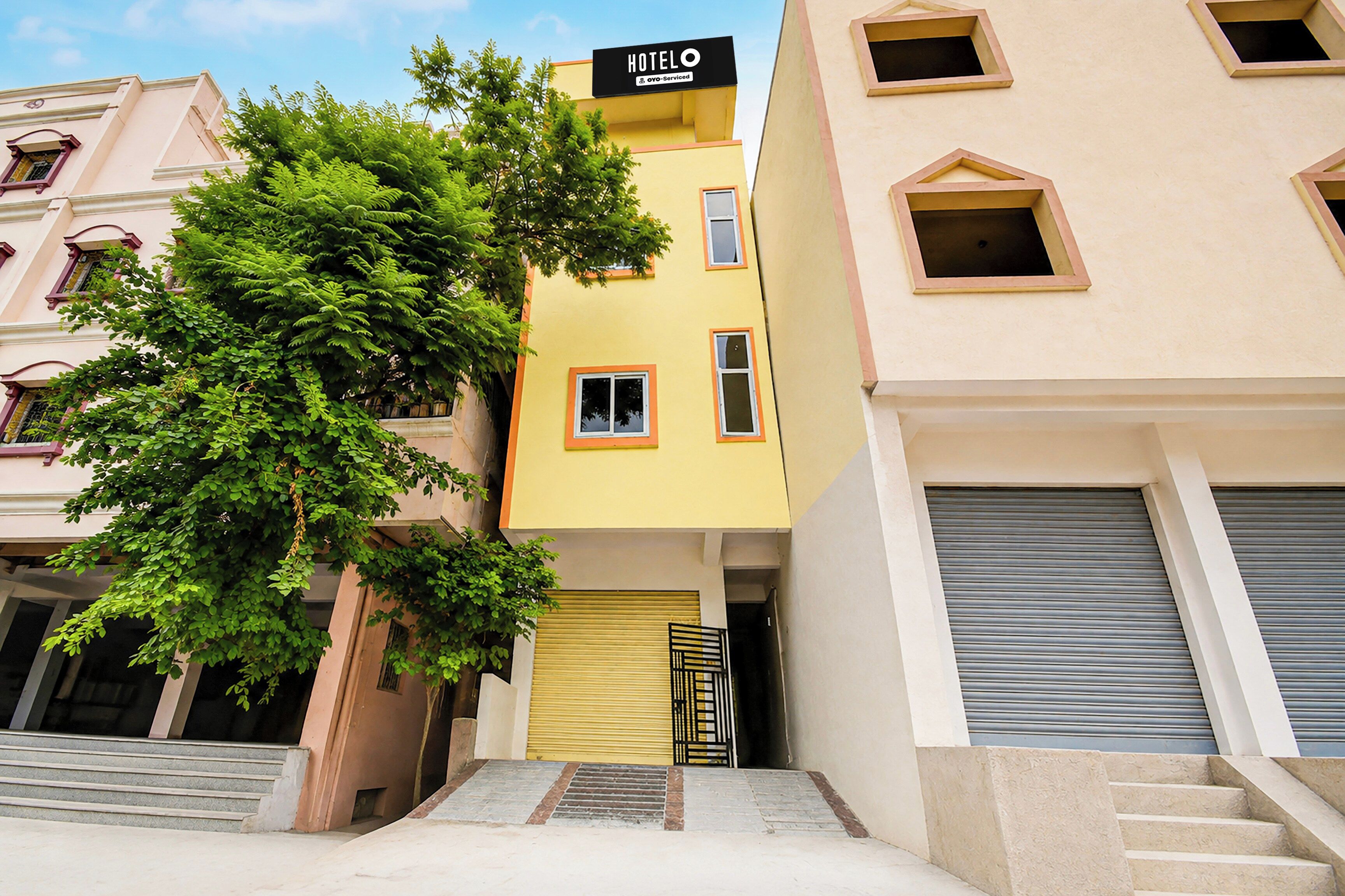 A multi-story hotel building with a yellow facade, a sign indicating it is a hotel, and a tree in front.