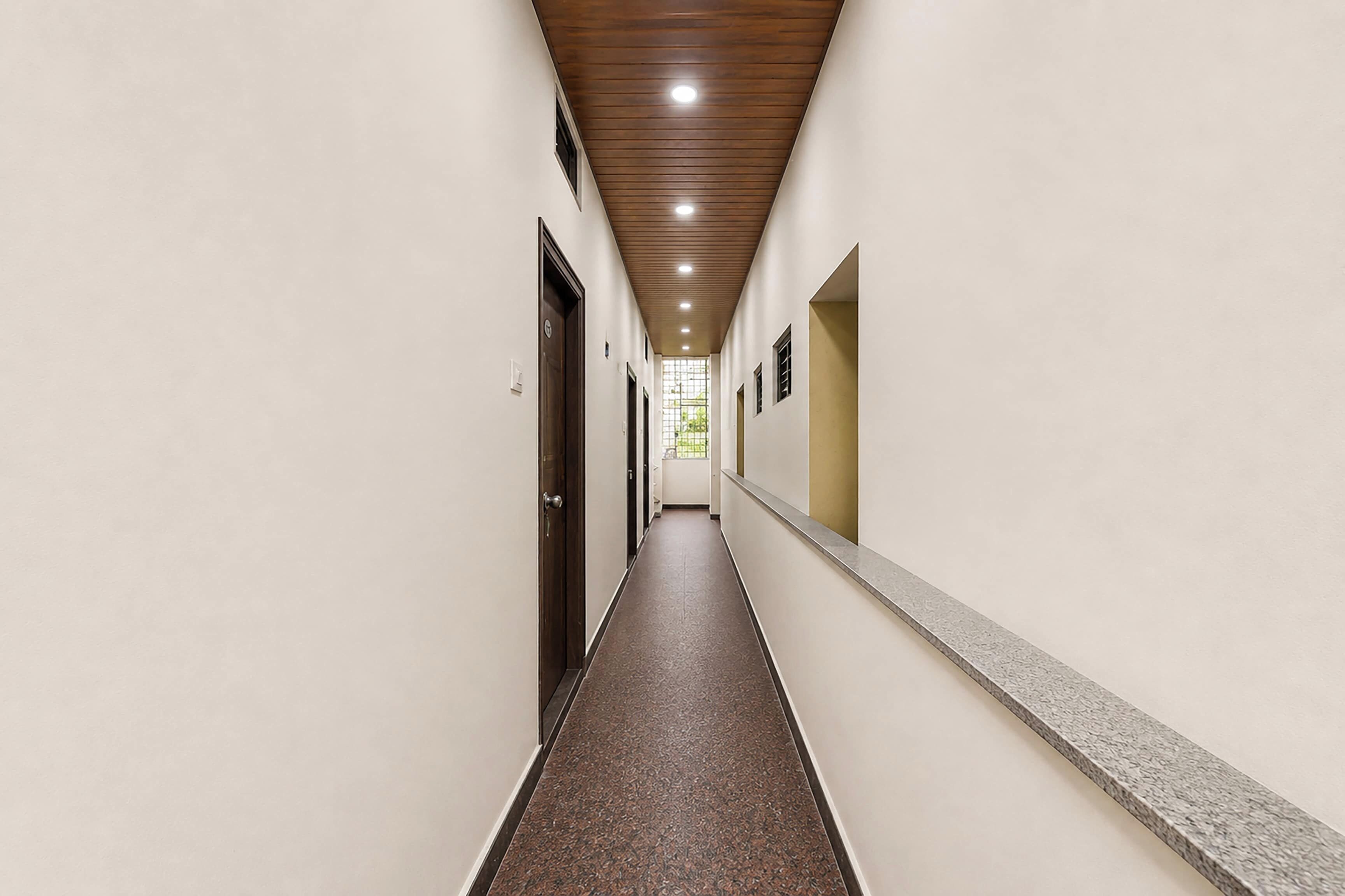 Un largo y estrecho pasillo con techo de madera, paredes blancas y suelo estampado.