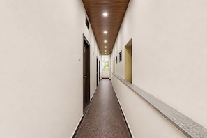 Un largo y estrecho pasillo con techo de madera, paredes blancas y suelo estampado.