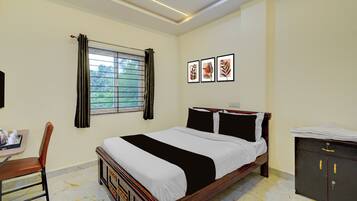 Habitación de hotel con cama, escritorio con silla, ventana con cortinas y cuadros en la pared.