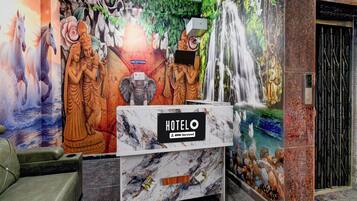 A hotel reception desk with a marble top, a sign indicating 'HOTEL' and 'o-v-serviced', and a mural depicting various figures and a waterfall.