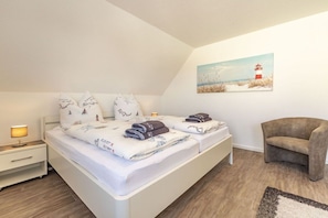 A bedroom with a bed, a nightstand, a chair, and a painting on the wall. - Dike view left||Norddeich (Norddeich)