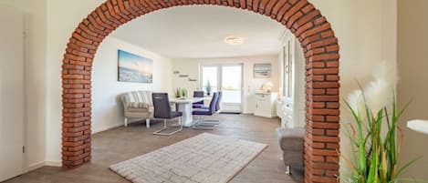 A living room with a brick archway, a dining area with a table and chairs, and a view of the outside.