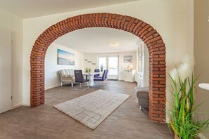 A living room with a brick archway, a dining area with a table and chairs, and a view of the outside. - Dike view left||Norddeich (Norddeich)