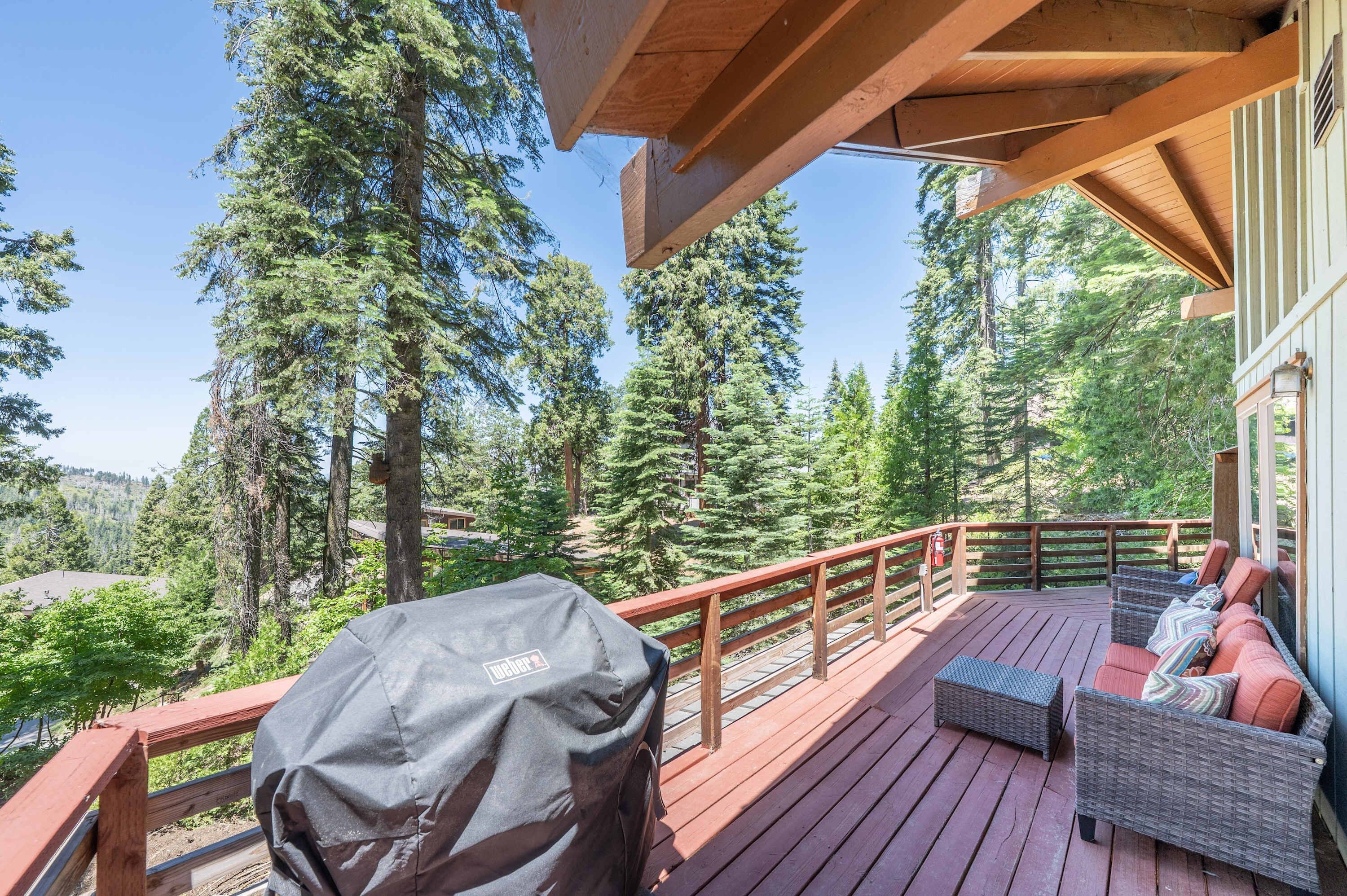A wooden deck with outdoor furniture and a barbecue grill, surrounded by tall trees.