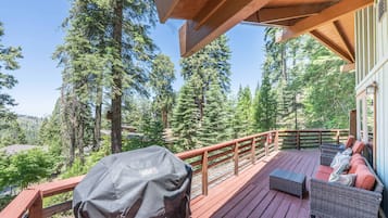 A wooden deck with outdoor furniture and a barbecue grill, surrounded by tall trees.