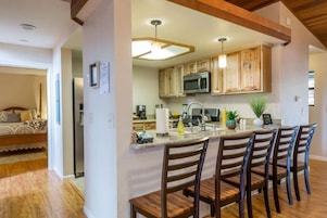 Una cocina moderna con armarios de madera, un microondas integrado y una barra con cuatro sillas.