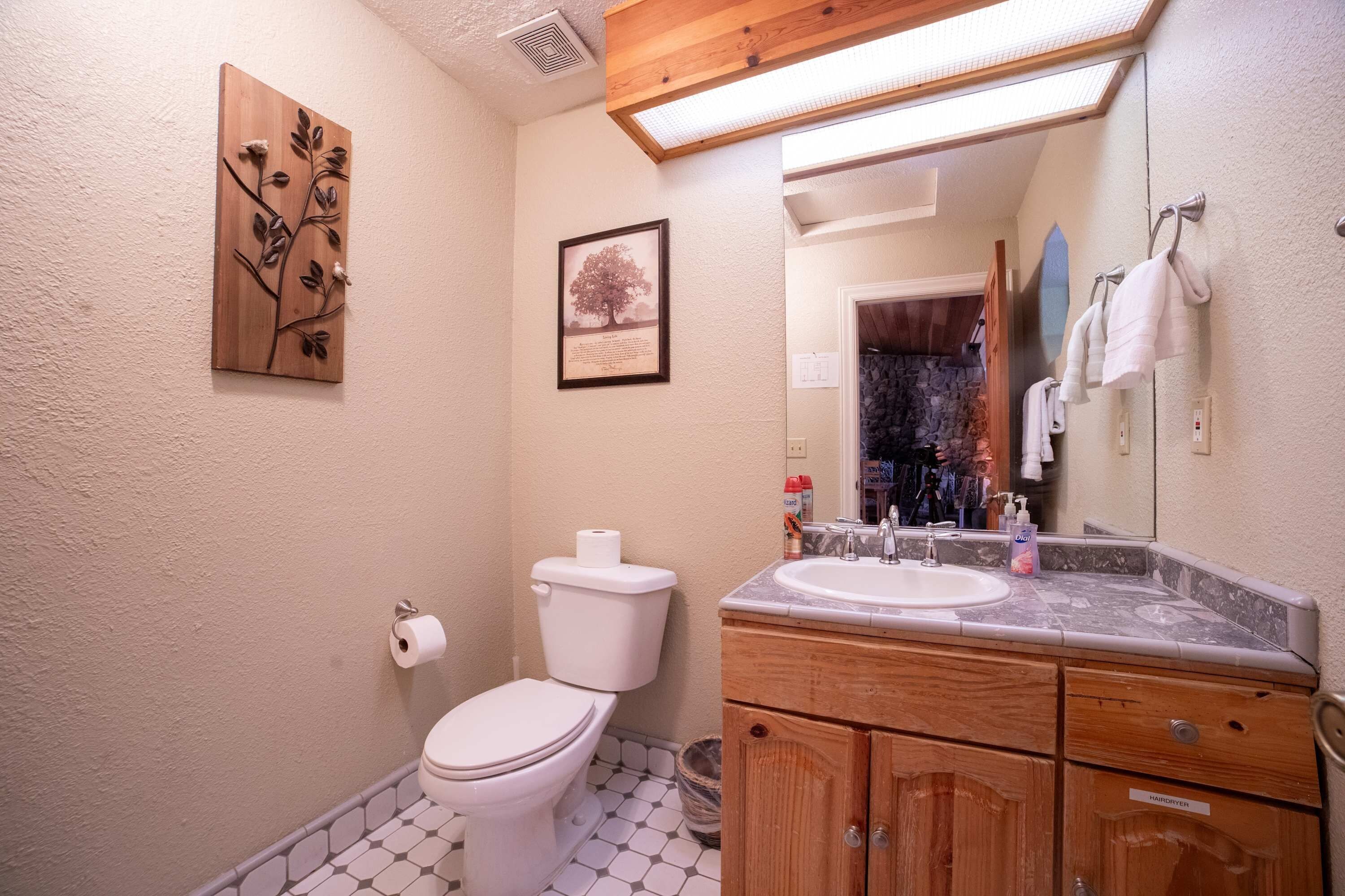 A bathroom with a toilet, sink, wooden cabinets, a mirror, and a shower area.