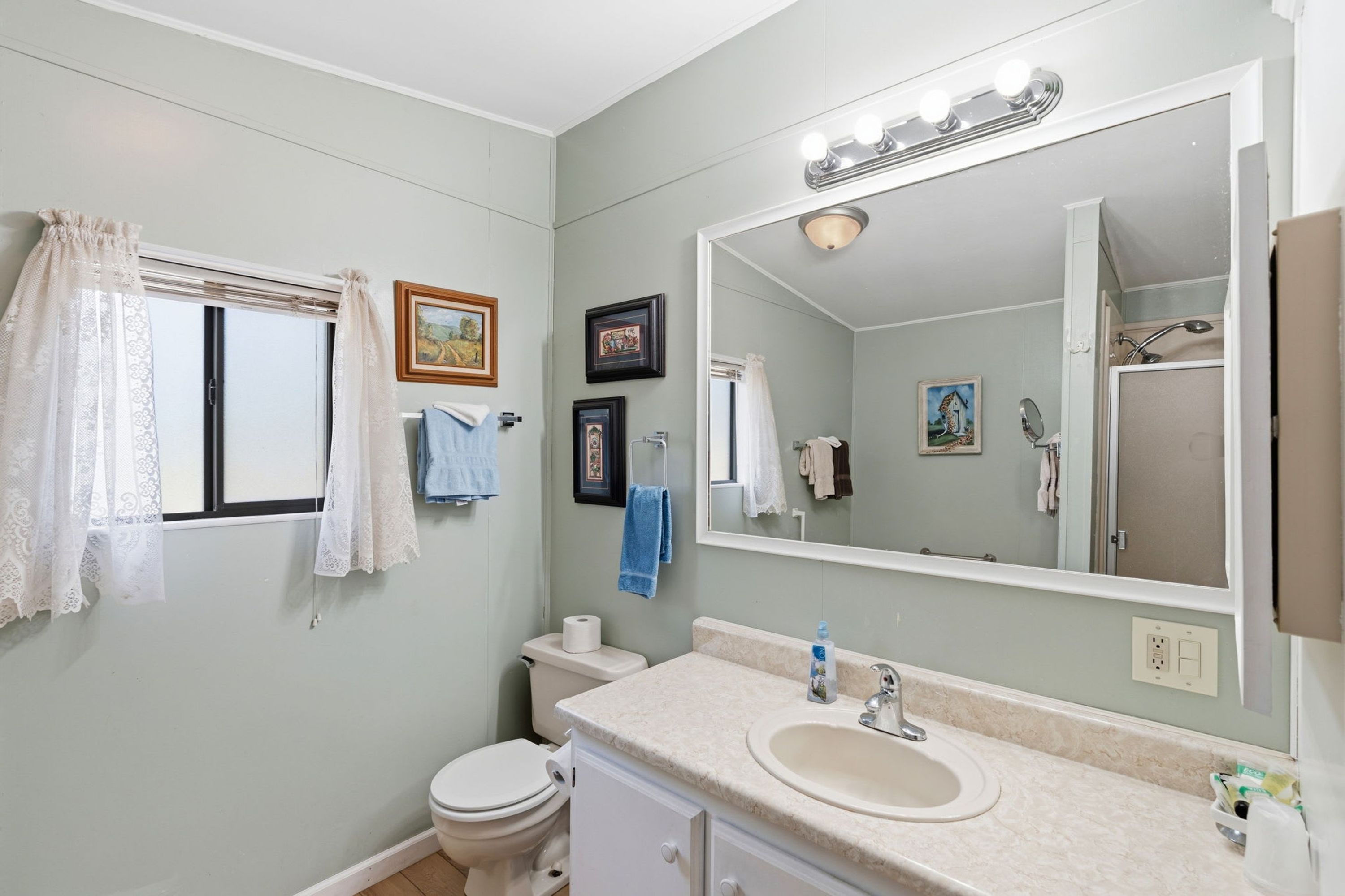 A bathroom with a toilet, sink, and mirror. There are towels and a picture frame on the wall.