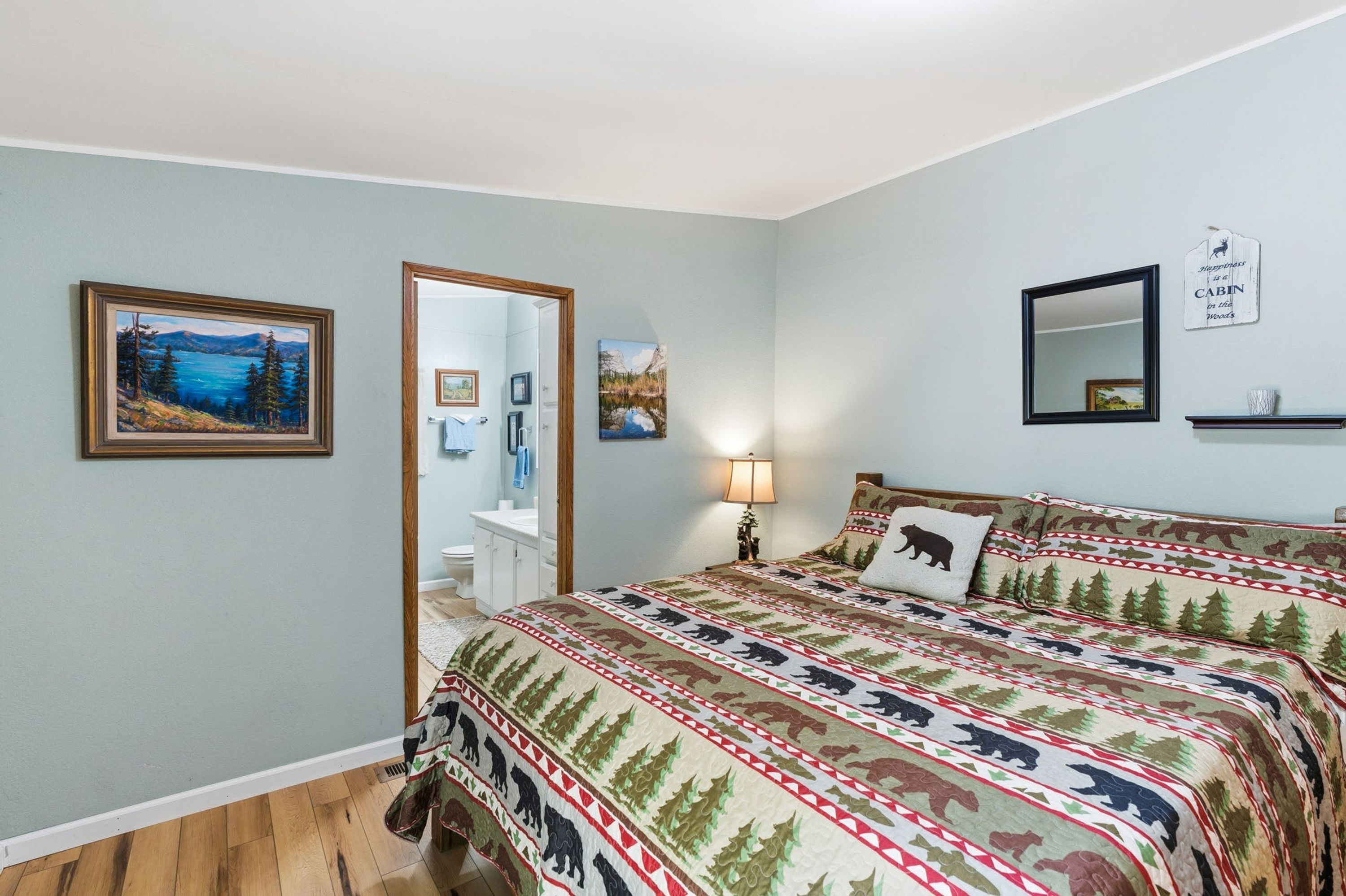 Quarto com cama, cômoda, espelho e duas pinturas na parede.