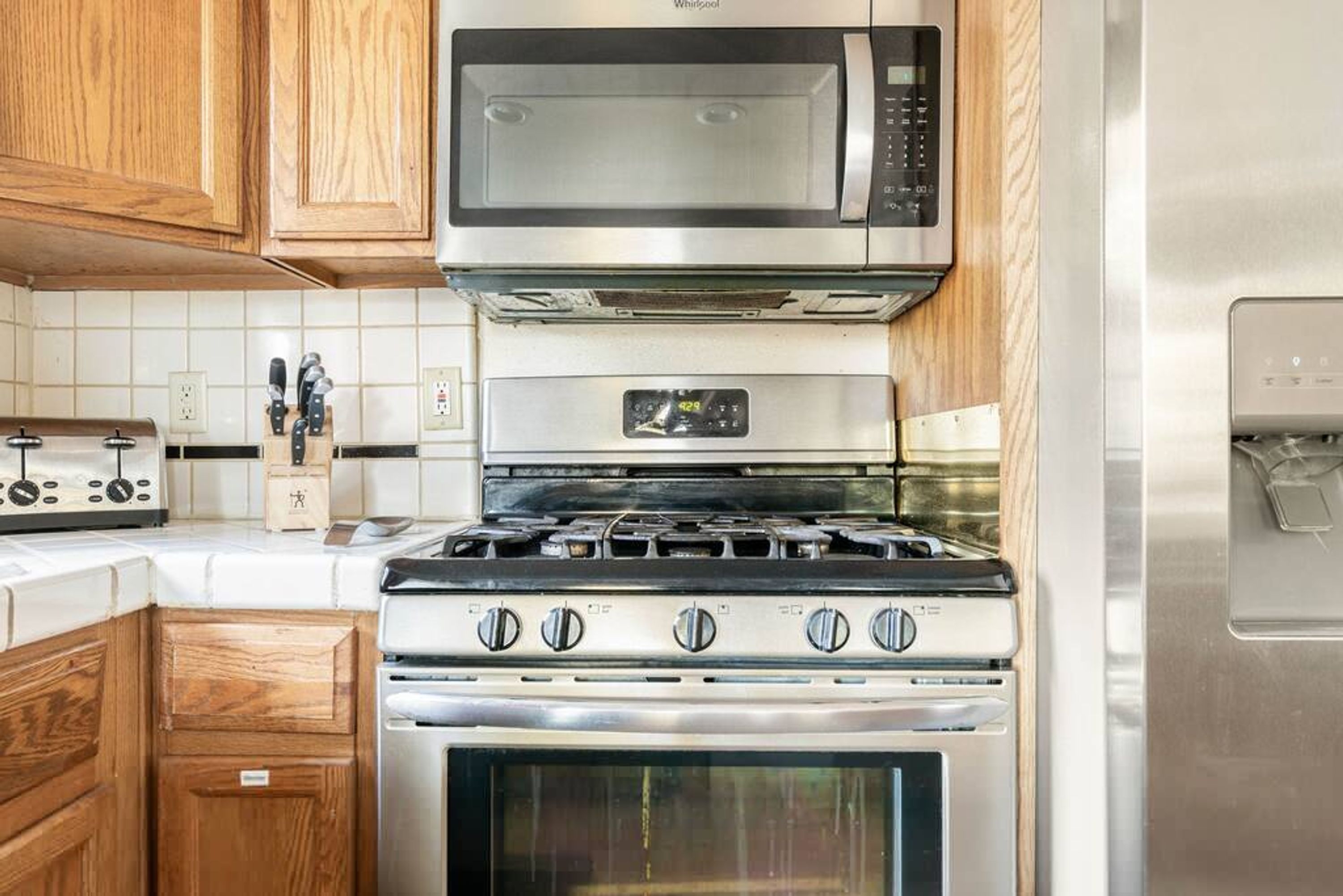 A kitchen with a stainless steel microwave, a gas stove, and wooden cabinets.