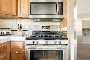 A kitchen with a stainless steel microwave, a gas stove, and wooden cabinets. - Inside Yosemite Park- Scenic Cascade (Yosemite National Park)
