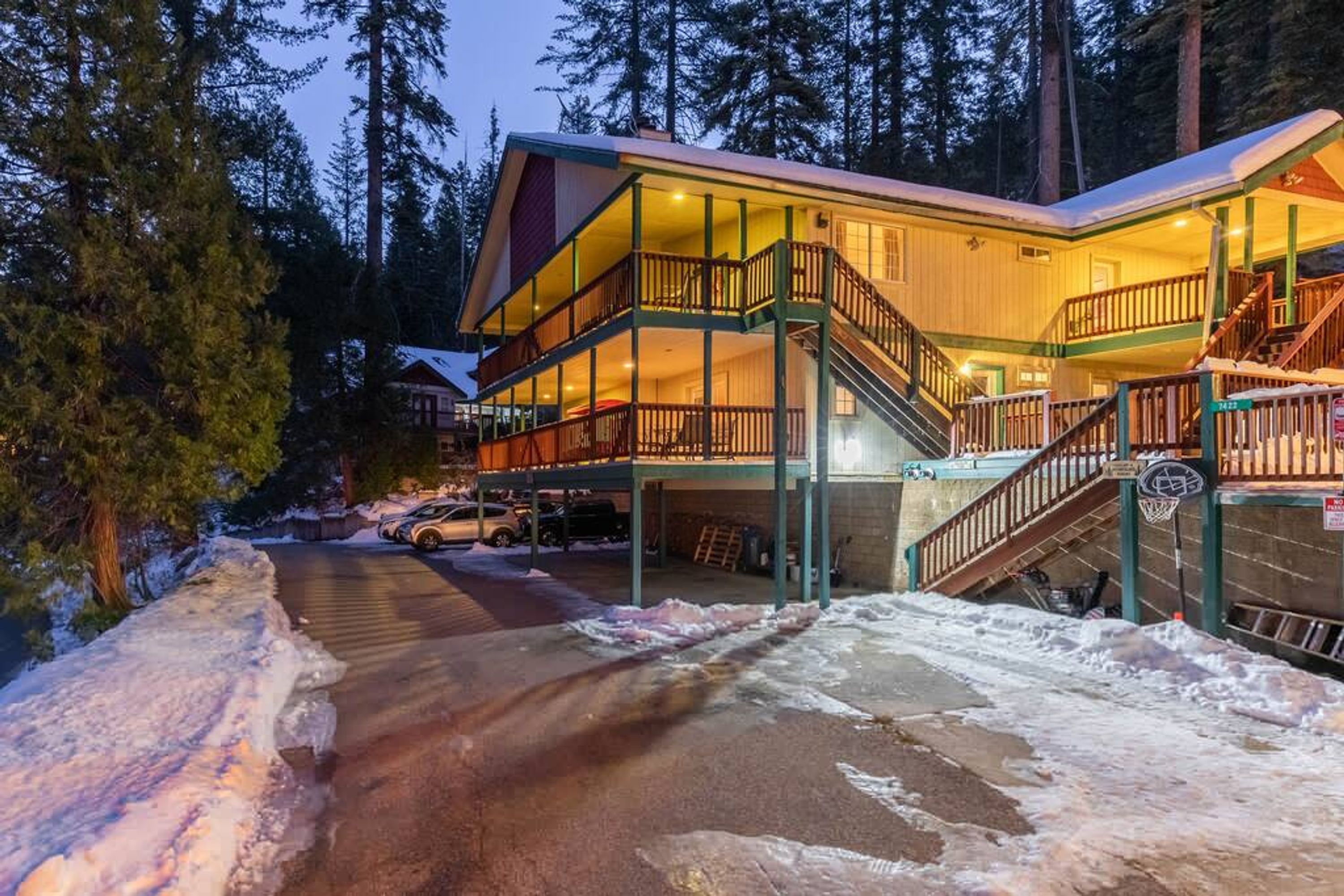 A multi-story lodge with a balcony and a staircase leading to the upper floor, surrounded by snow and trees.
