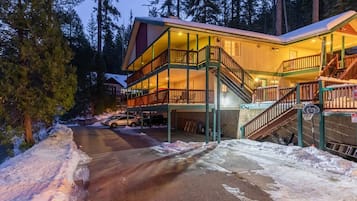 A multi-story lodge with a balcony and a staircase leading to the upper floor, surrounded by snow and trees.