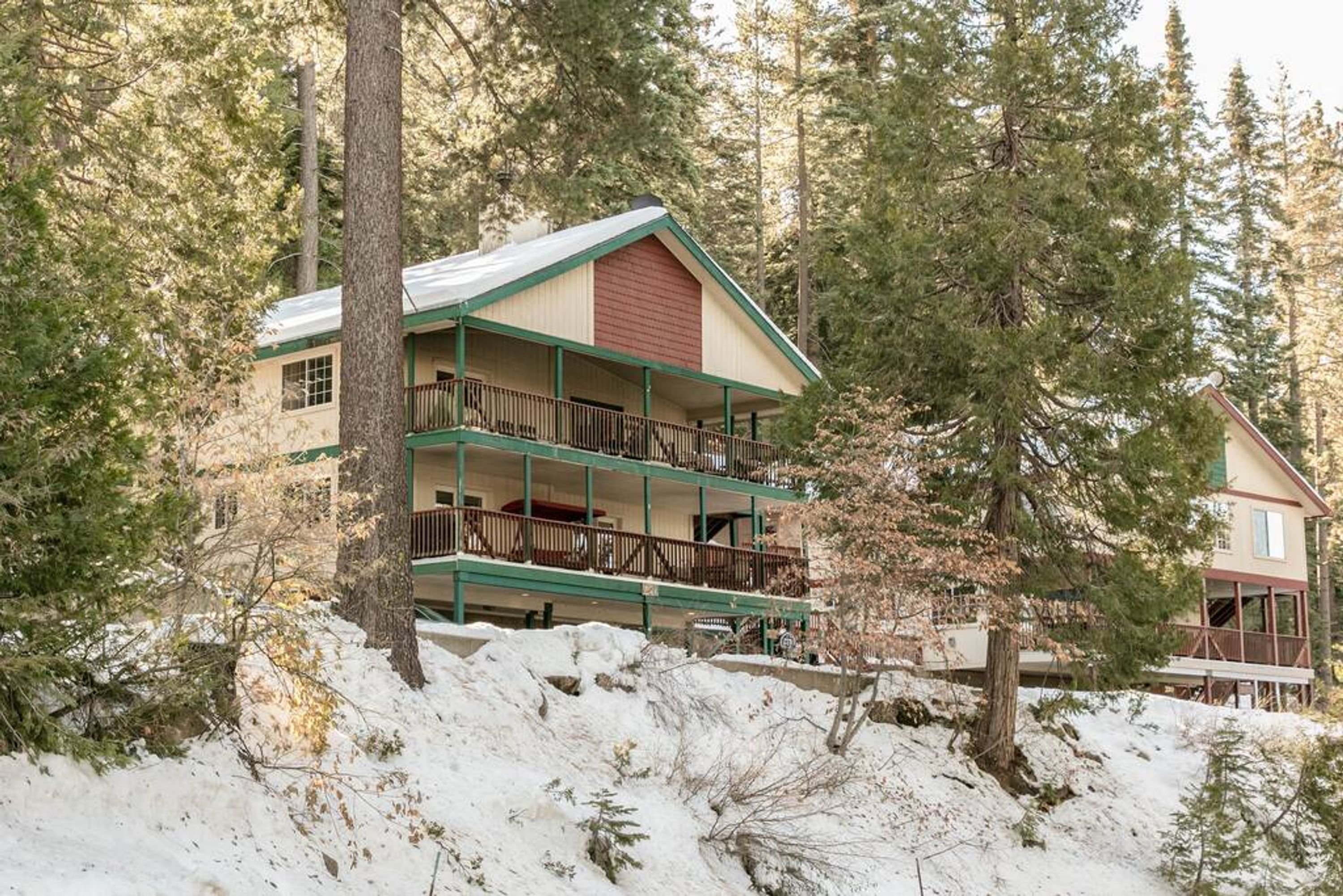 A two-story lodge with a balcony on the upper floor, surrounded by trees and snow.