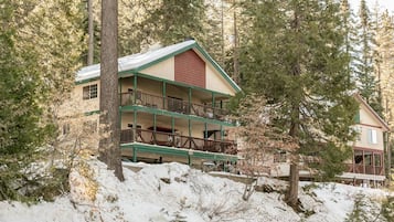 A two-story lodge with a balcony on the upper floor, surrounded by trees and snow.