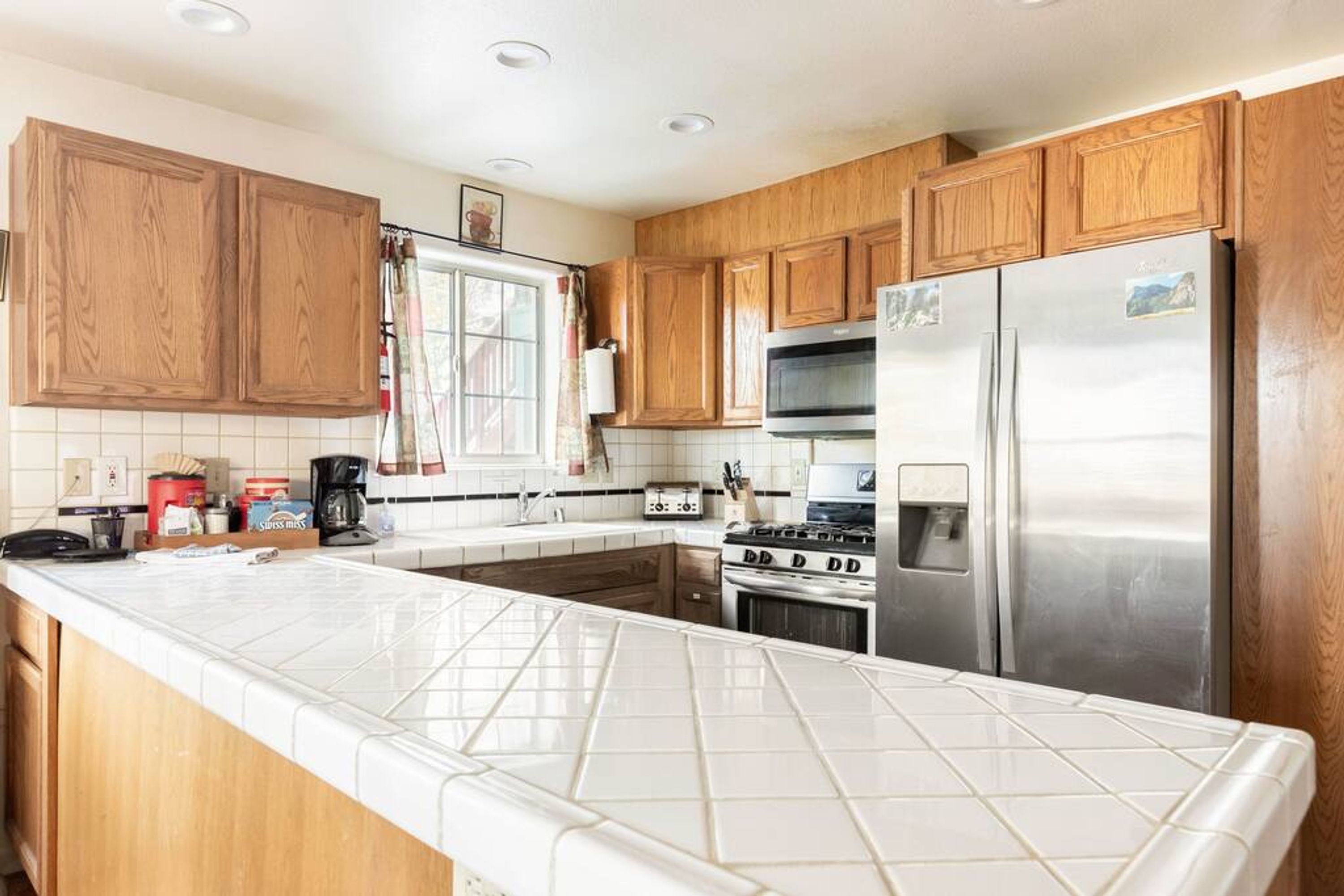 A kitchen with wooden cabinets, a stainless steel refrigerator, a stove, and a microwave.
