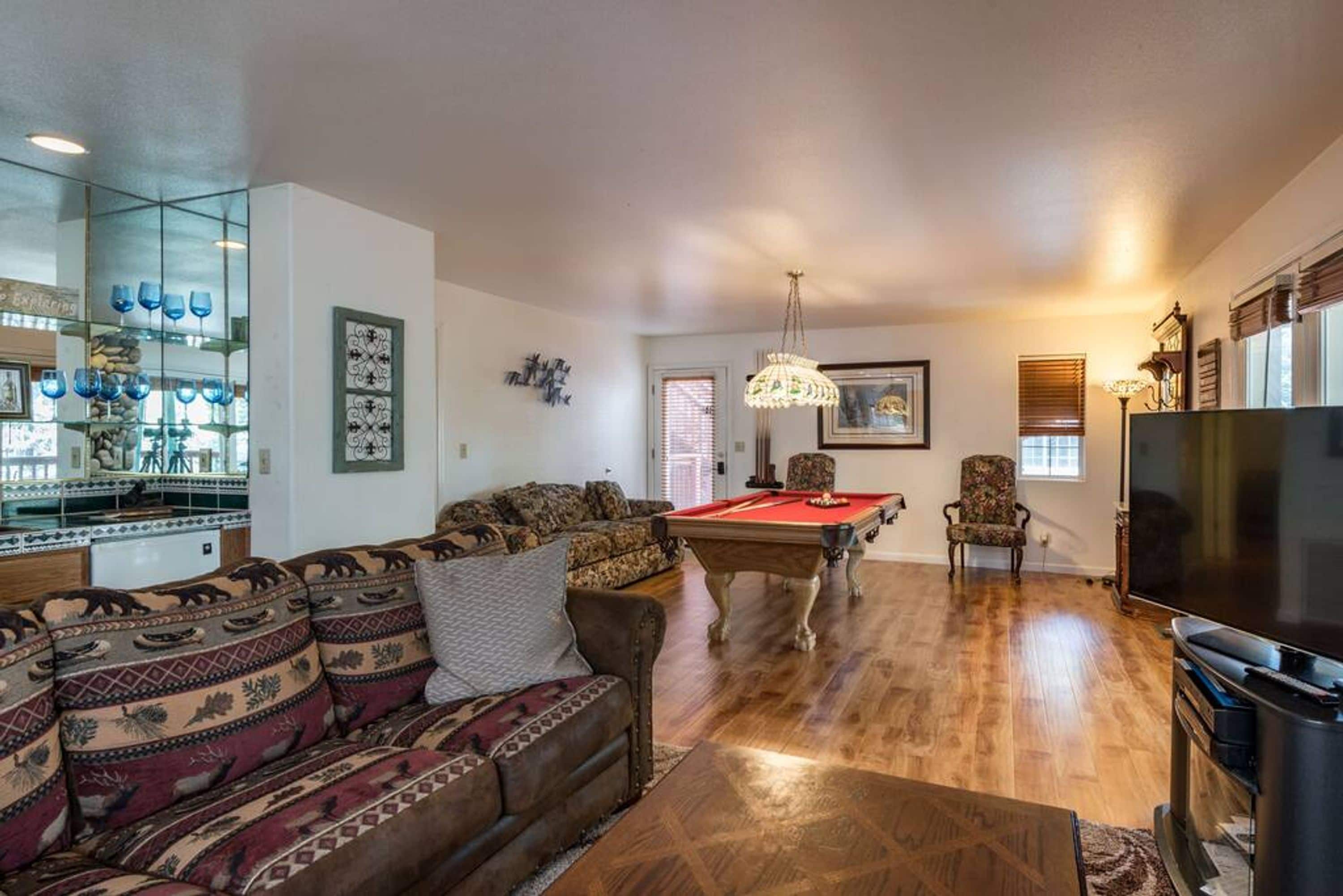 A living room with a pool table, a sofa, a television, and a glass display case with blue glassware.