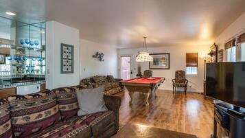 A living room with a pool table, a sofa, a television, and a glass display case with blue glassware.