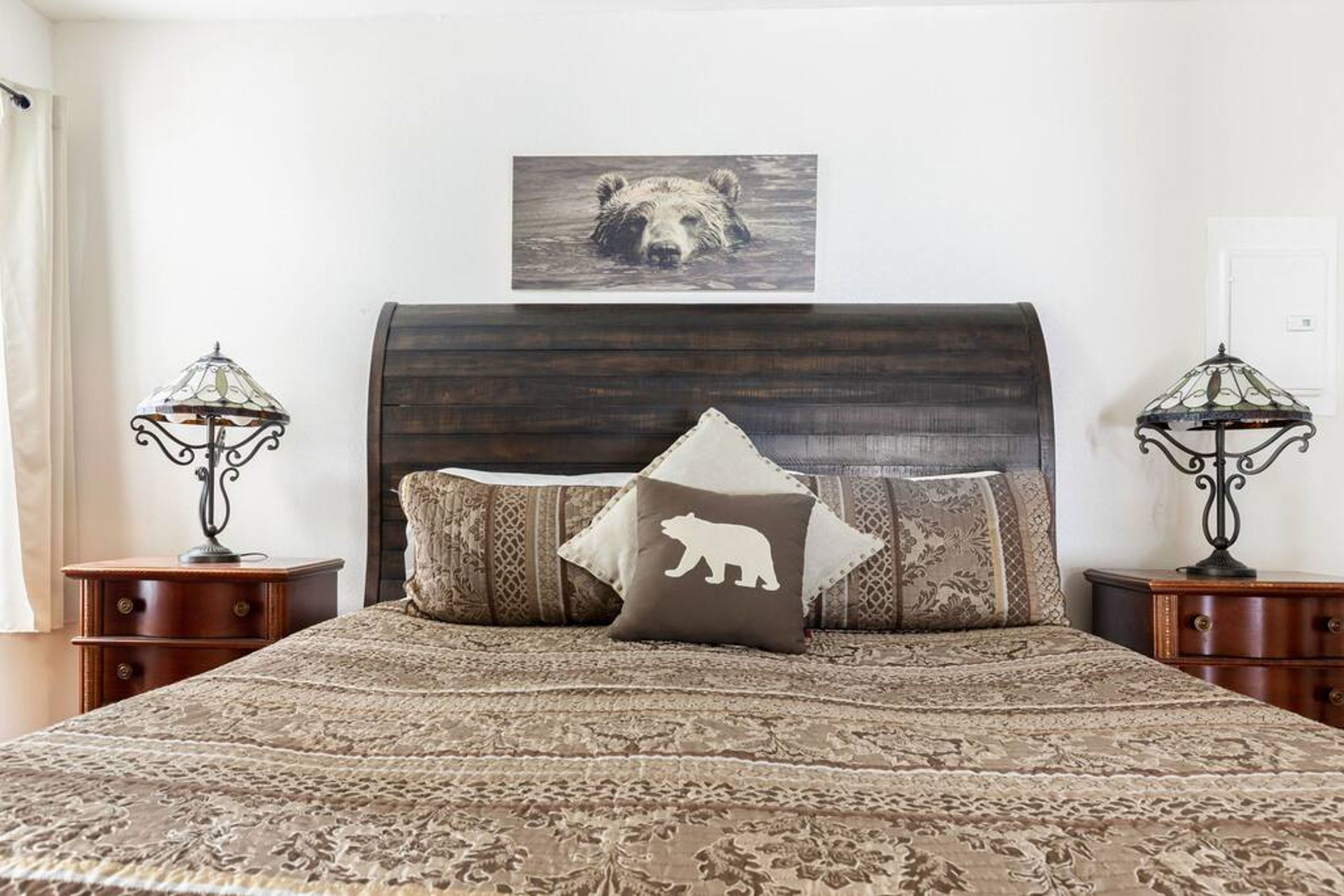 Un dormitorio con una cama grande, dos mesitas de noche, un cabecero y un cuadro colgado en la pared de un oso.