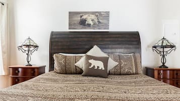 A bedroom with a large bed, two nightstands, a headboard, and a wall-mounted picture of a bear.