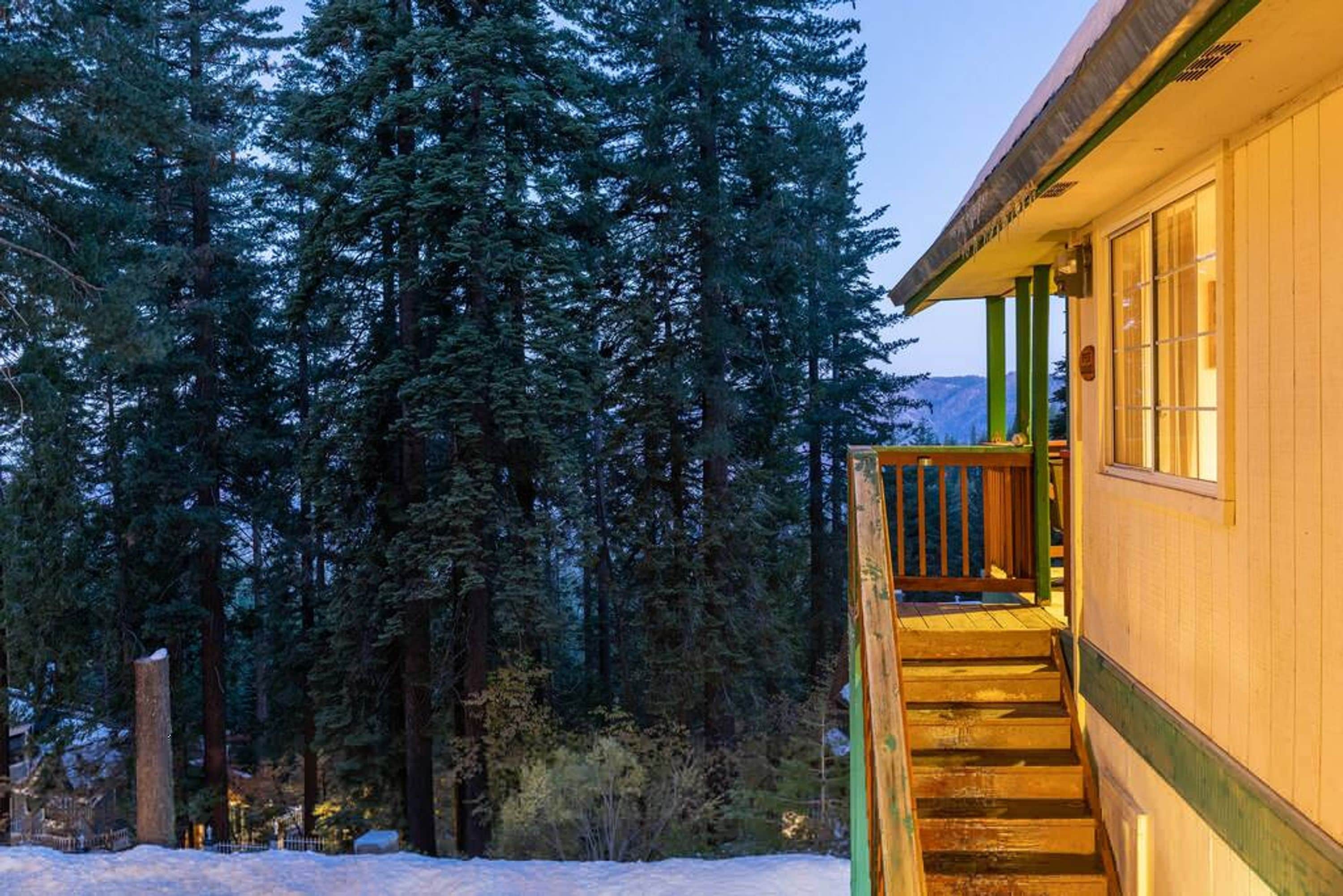 A wooden building with a staircase leading to a balcony, surrounded by tall evergreen trees.
