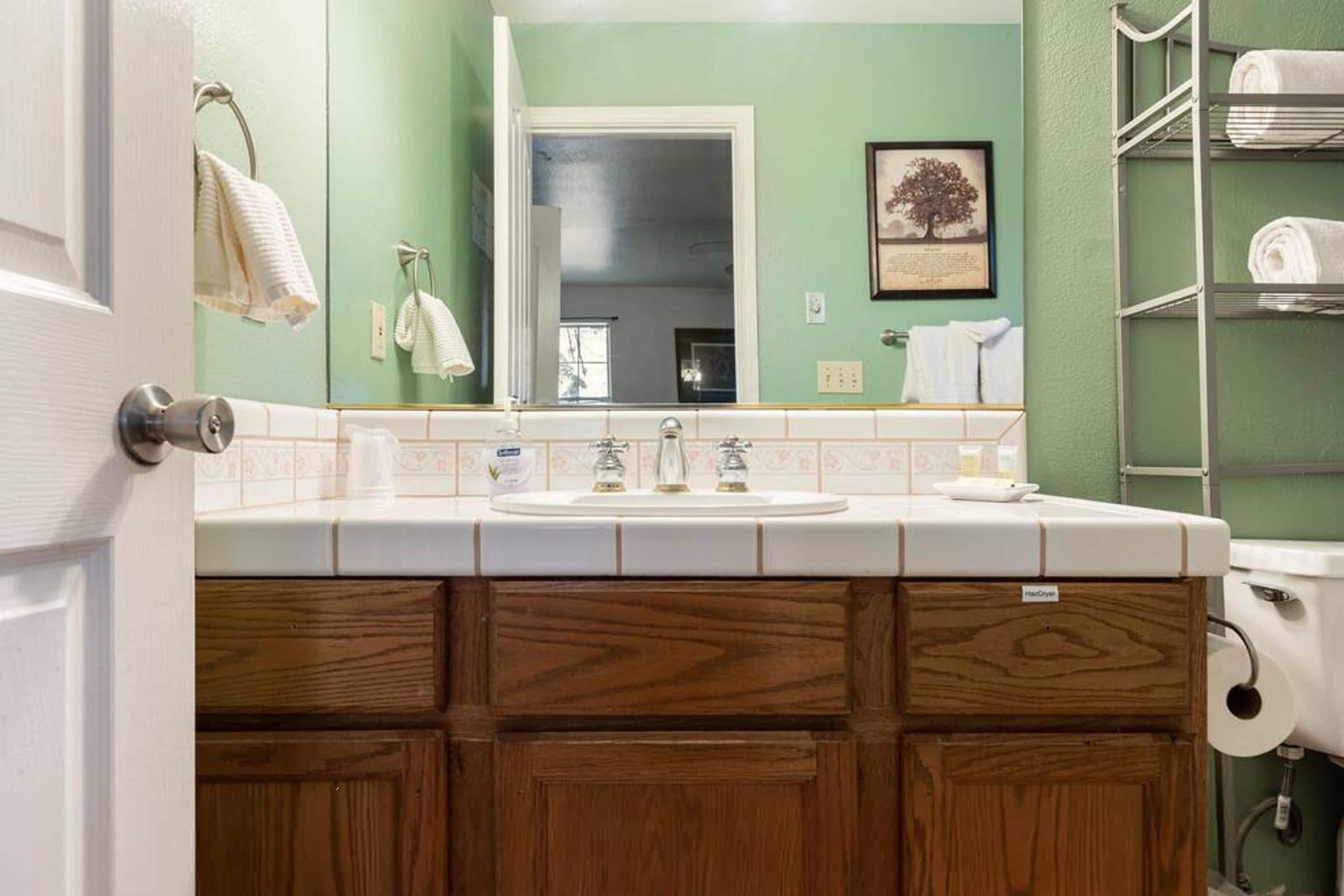 A bathroom with a wooden vanity, a sink, and a toilet. There are towels hanging on the wall and a framed picture above the mirror.