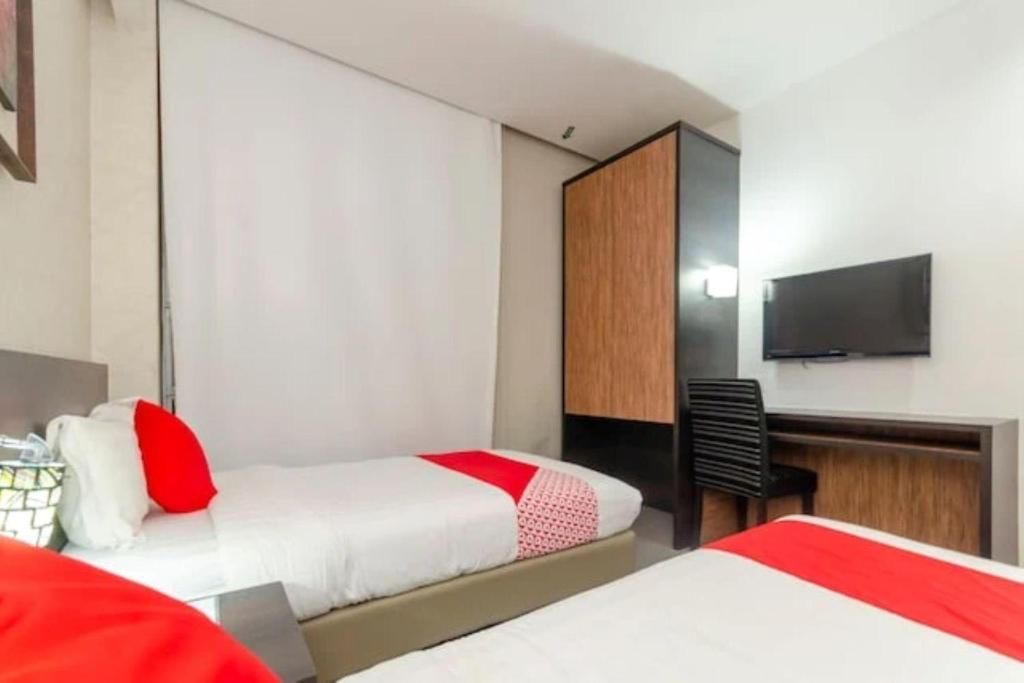 Habitación de hotel con dos camas, un escritorio, una silla y un televisor en la pared.