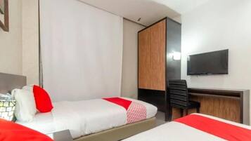 Habitación de hotel con dos camas, un escritorio, una silla y un televisor en la pared.