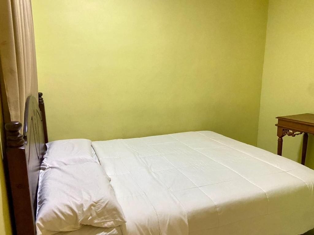 A bed with a white mattress and pillows, a wooden headboard, and a small wooden nightstand to the right.