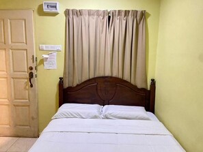 Una habitación con una cama de madera, una puerta, un interruptor de luz y una lámpara fijada a la pared.