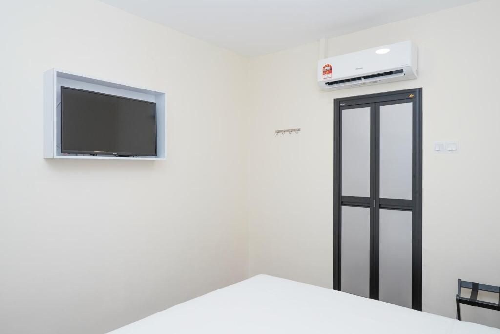 A room with a white table, a mounted TV, a door with a black frame, and an air conditioning unit.