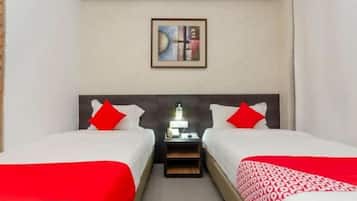 Habitación de hotel con dos camas, cada una con ropa de cama roja, una mesita de noche con lámpara y un cuadro en la pared.