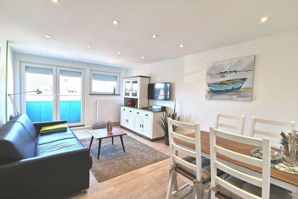 A modern living room with a sofa, a dining table with chairs, a TV, and a painting on the wall.